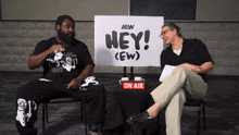 two men are sitting in front of a sign that says hey ( ew )