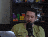 a man in a green shirt is talking into a microphone in front of a shelf with a nintendo soldier magazine on it