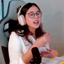 a woman wearing headphones and glasses is sitting in front of a microphone ..