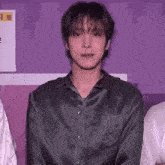 a young man in a green shirt is standing in front of a purple wall and looking at the camera .