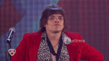 a man in a red jacket stands in front of a microphone with eltrece on the bottom right