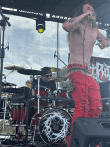 a shirtless man singing into a microphone wearing a belt that says danger zone on it