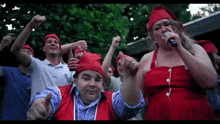 a woman in a red dress is singing into a microphone in front of a crowd of people wearing red hats