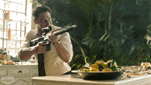 a man holding a gun in a kitchen with a bowl of lemons on the counter and a prime arrow in the corner