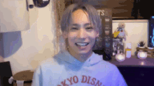 a young man wearing a tokyo disn sweatshirt is smiling .