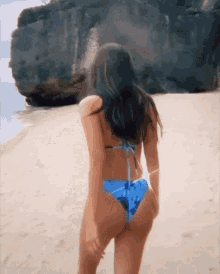 a woman in a bikini is walking on a sandy beach .