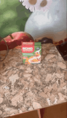 a box of rcho sits on a table next to an apple