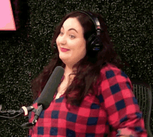 a woman wearing headphones and a plaid shirt is smiling in front of a microphone