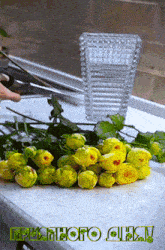 a bunch of yellow flowers are on a counter with a glass vase in the background