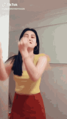 a woman in a yellow top and red skirt is dancing on a tik tok video