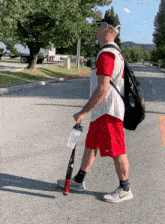 a man walking down a street holding a bat and a bottle of water