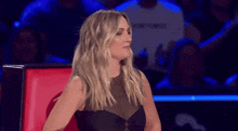 a woman in a black dress is sitting in a red chair in front of a crowd