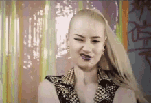 a woman with blonde hair and purple lipstick is wearing a studded jacket and earrings .