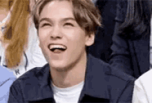 a young man in a blue jacket is laughing in a crowd of people .
