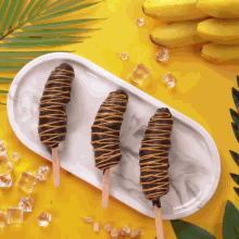 three chocolate covered bananas on a white plate on a yellow table