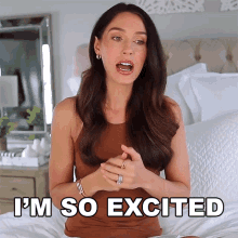 a woman is sitting on a bed with the words i 'm so excited above her