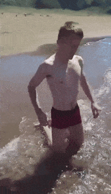 a shirtless man in red swim trunks is kneeling in the water
