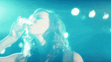 a woman is drinking from a glass in front of a blue light