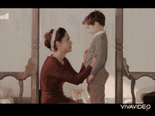a woman adjusts a boy 's pants in front of a sign that says vivavideo on it