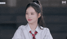 a girl with her eyes closed is wearing a white shirt and a red tie with the letter m on the bottom