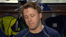 a hockey player in a locker room with a maple leafs jersey behind him