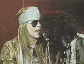 a woman singing into a microphone while wearing sunglasses and a bandana on her head