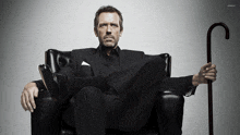 a man in a suit sits in a chair with his legs crossed and a cane