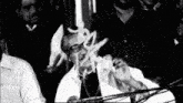 a man with glasses is giving a speech in front of a crowd .
