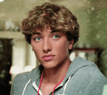 a young man wearing a grey hoodie with a red lanyard around his neck looks at the camera