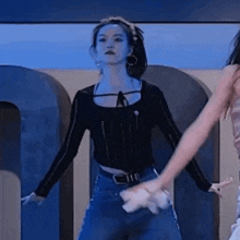 a woman in a black top and blue jeans is dancing on a stage in front of a large letter u .