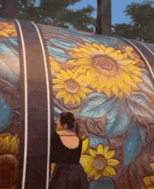 a woman stands in front of a large painting of sunflowers