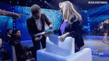 a man in a suit is pointing at a woman sitting in a chair on a television show .
