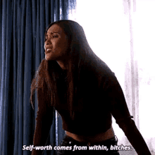 a woman is standing in front of a window and saying `` self-worth comes from within bitches '' .