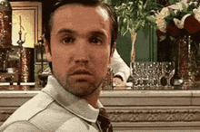 a man in a sweater and tie is standing in front of a bar looking at the camera .
