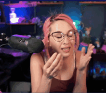 a woman with pink hair is wearing glasses and talking into a microphone