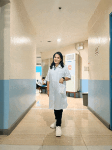 a woman in a lab coat is standing in a hallway with an exit sign on the wall