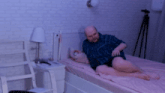 a bald man is laying on a bed with a pink blanket