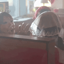 two women are sitting in a diner and one has a scarf over her head