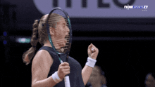 a woman is holding a tennis racquet in front of her face in front of a sign that says now sports 4