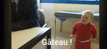 a baby in a red outfit is standing in front of a table .