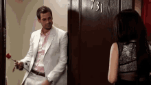 a man in a suit is holding a rose in front of a door that says 731
