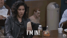 a woman in a leather jacket is sitting at a table and says i 'm in .