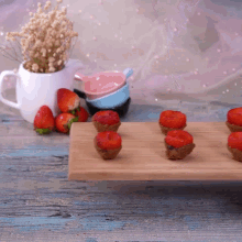 a tray of strawberries sits on a wooden table next to a vase of dried flowers