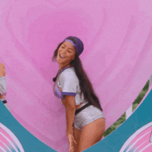 a woman in a baseball uniform is standing in front of a pink heart shaped wall .