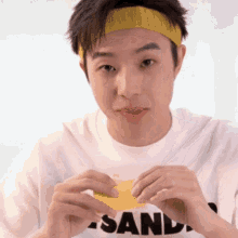 a man wearing a yellow headband and a white shirt that says sand on it
