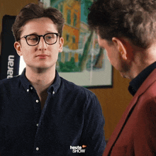 a man wearing glasses talks to another man with the words heute show below him