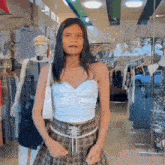 a woman wearing a plaid skirt and a white top is standing in front of a store window .