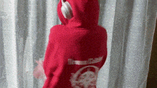 a person wearing a red hoodie and headphones is standing in front of a window .