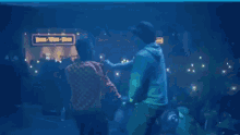 two men are dancing on a stage in front of a crowd in a dark room .