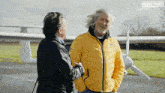 a man in a yellow jacket is talking to another man in front of a plane